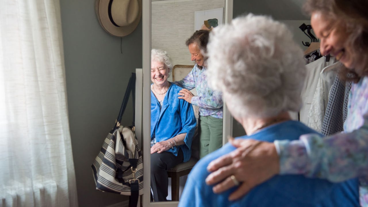 Photo of two seniors looking into full-body mirror, smiling