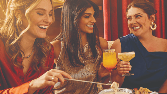 Melting Pot 50th anniversary photo, featuring three people enjoying celebratory drinks and fondue